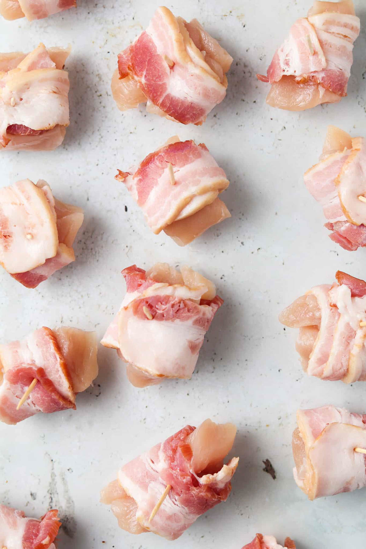 Raw bacon wrapped chicken bites with tooth picks on a tray.