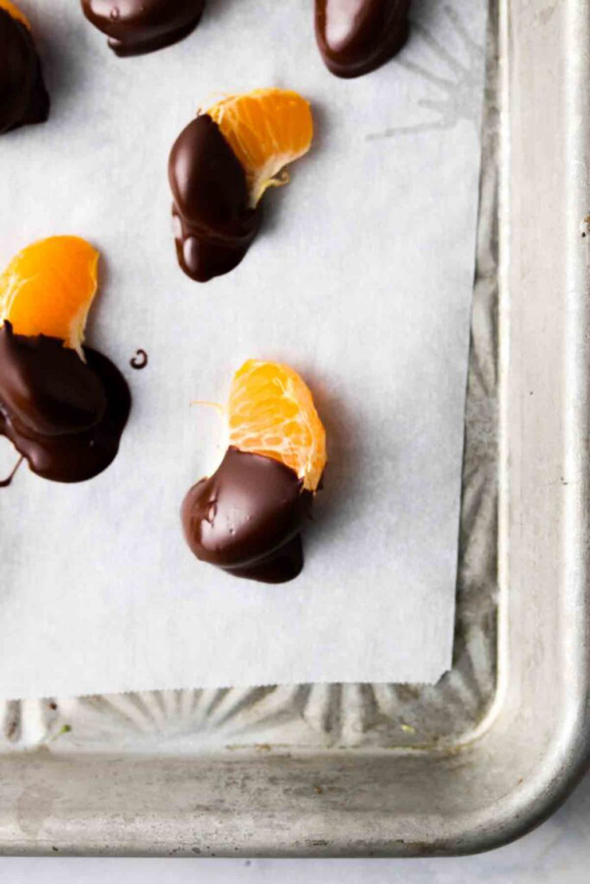 Chocolate dipped orange wedges on wax paper on a baking sheet.