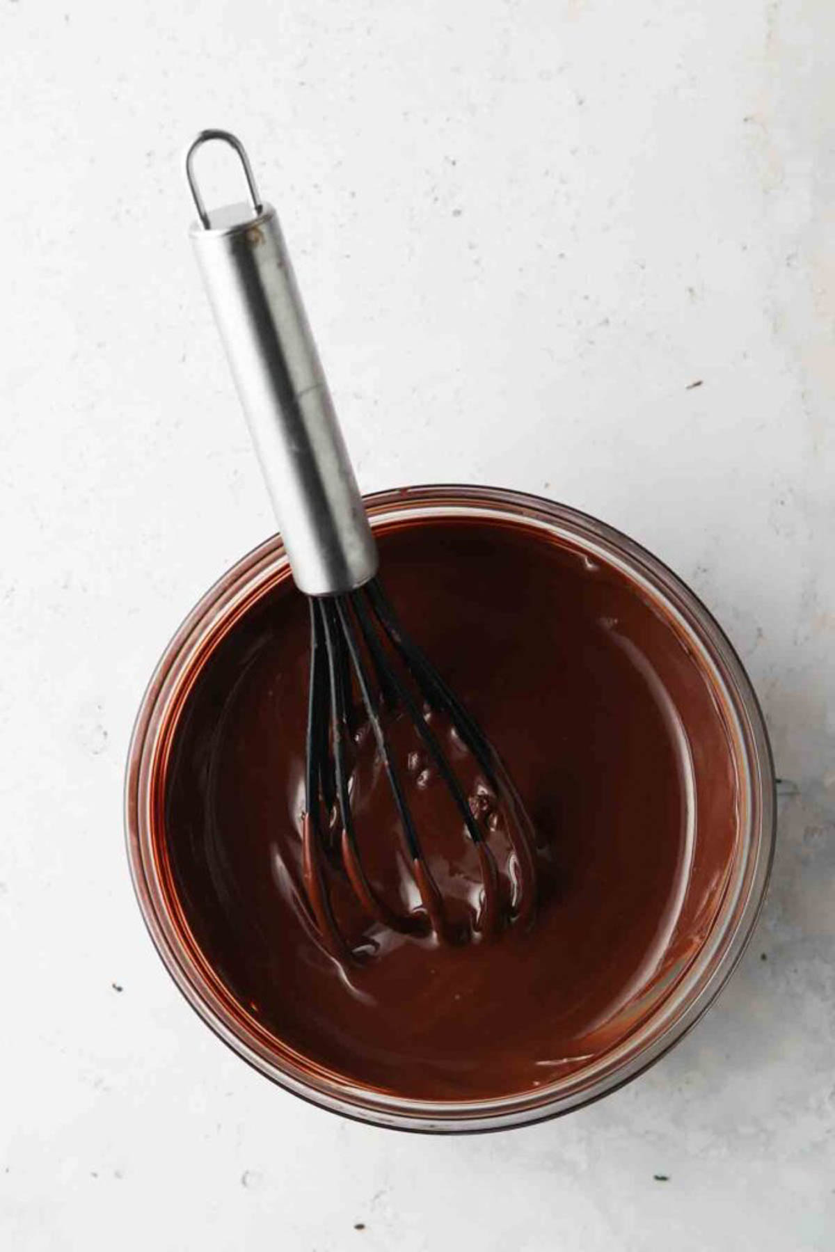 Melted chocolate in a glass bowl with a whisk.