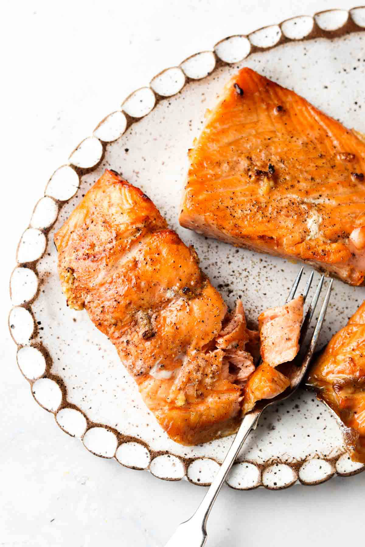 Air fried salmon filets on a white platter with freshly cracked pepper on top and a fork on the side. 