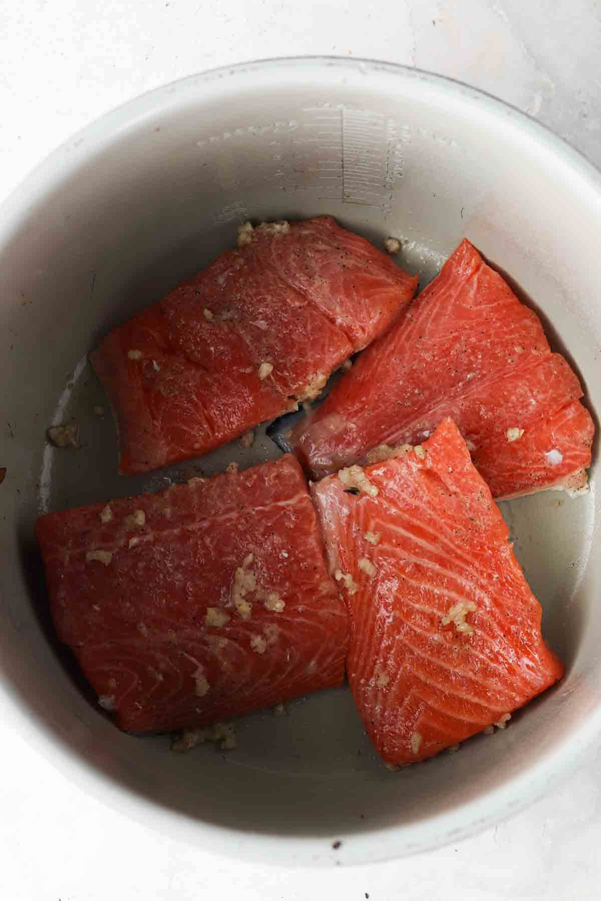 Salmon filets cut up in the air fryer facing up with seasoning and herbs on top.
