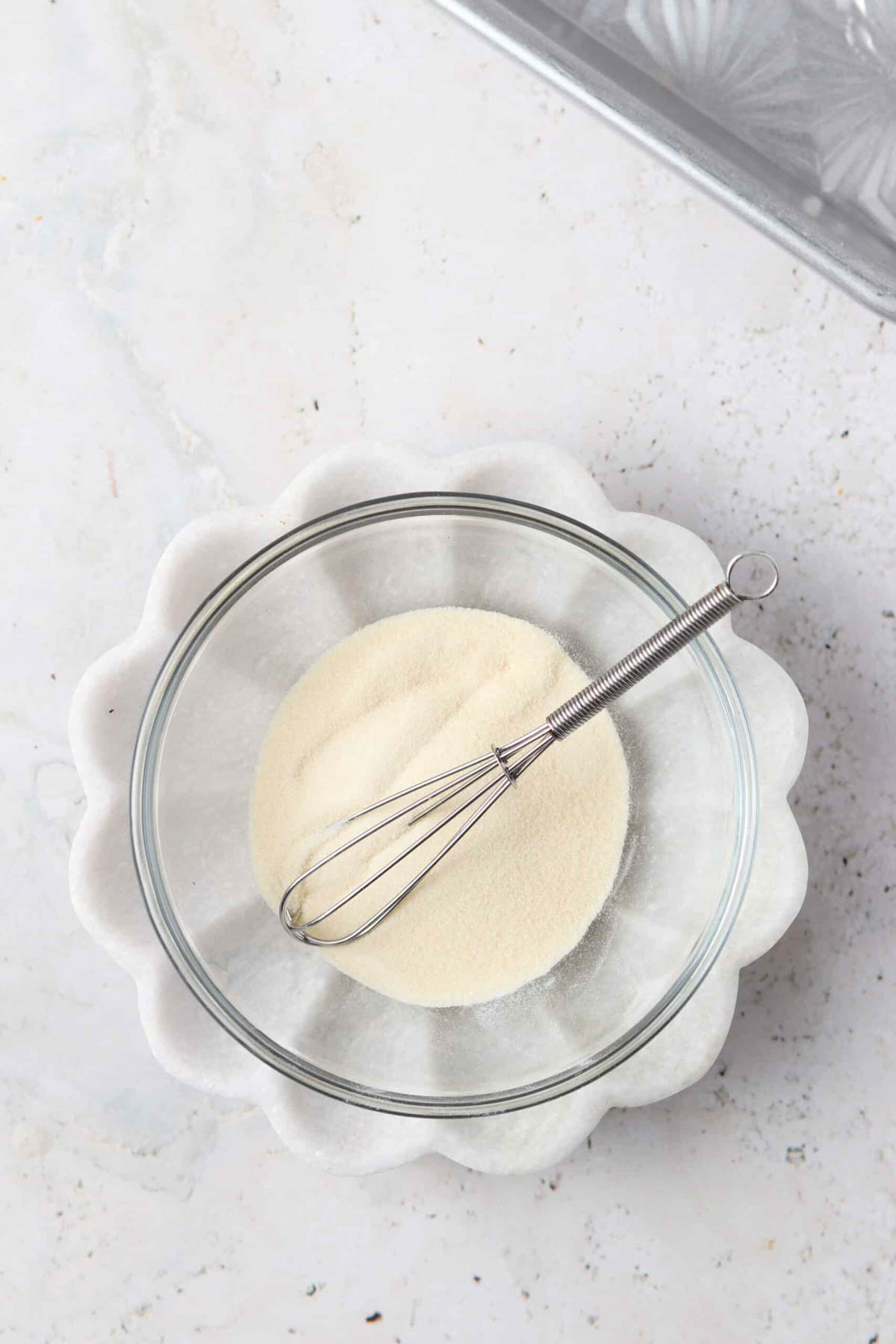 Gelatin and water in a glass mixing bowl with a small whisk.