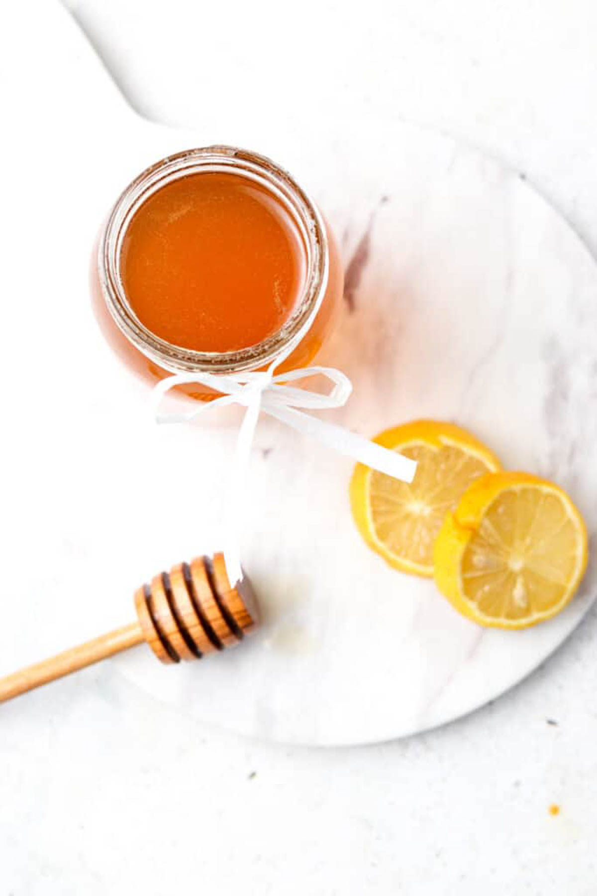 Honey simple syrup in a glass mason jar with lid off on a platter with lemon slices. 