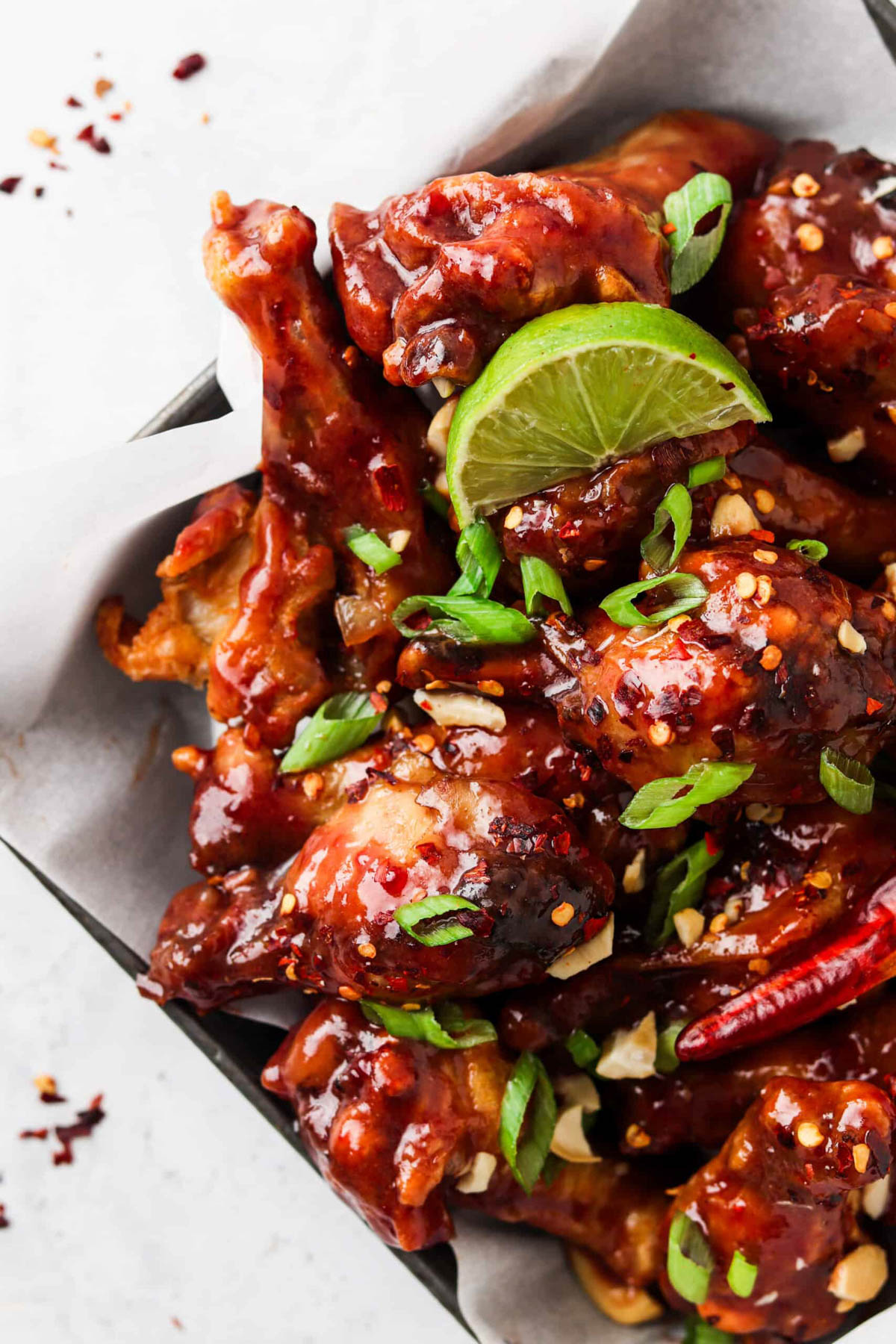 Peanut butter and jelly chicken wings on a plate with limes and garnished with red pepper flakes and scallions.