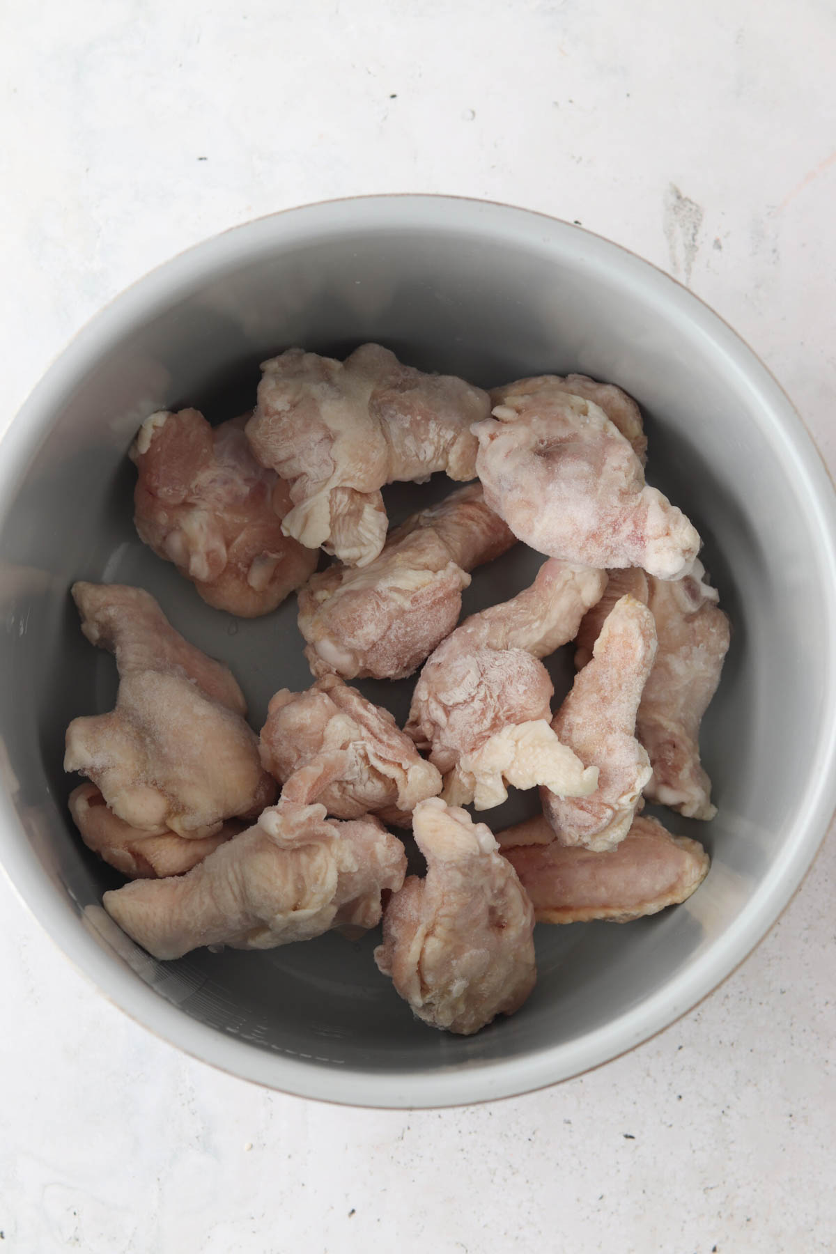 Frozen chicken wings in an air fryer basket.