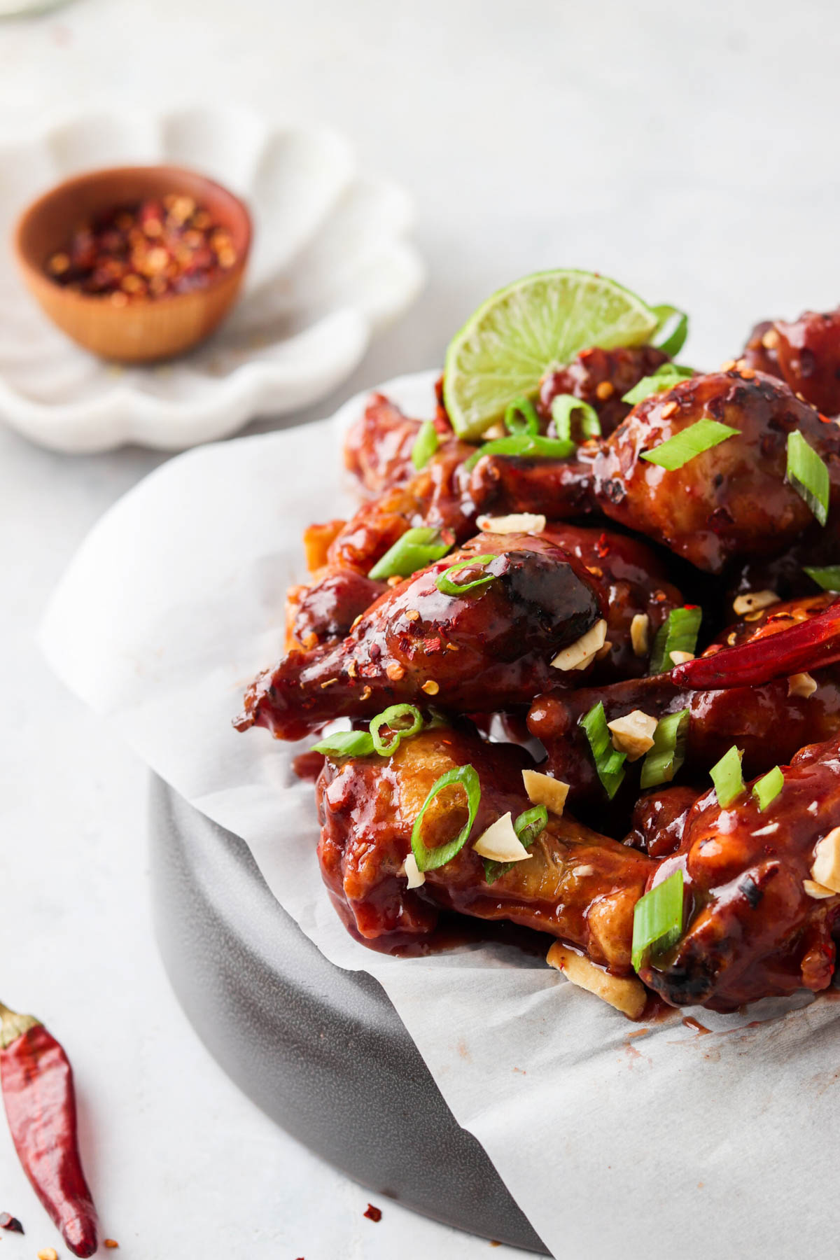 Peanut butter and jelly wings on a plate and garnished with green onions, red pepper flakes, and lime.