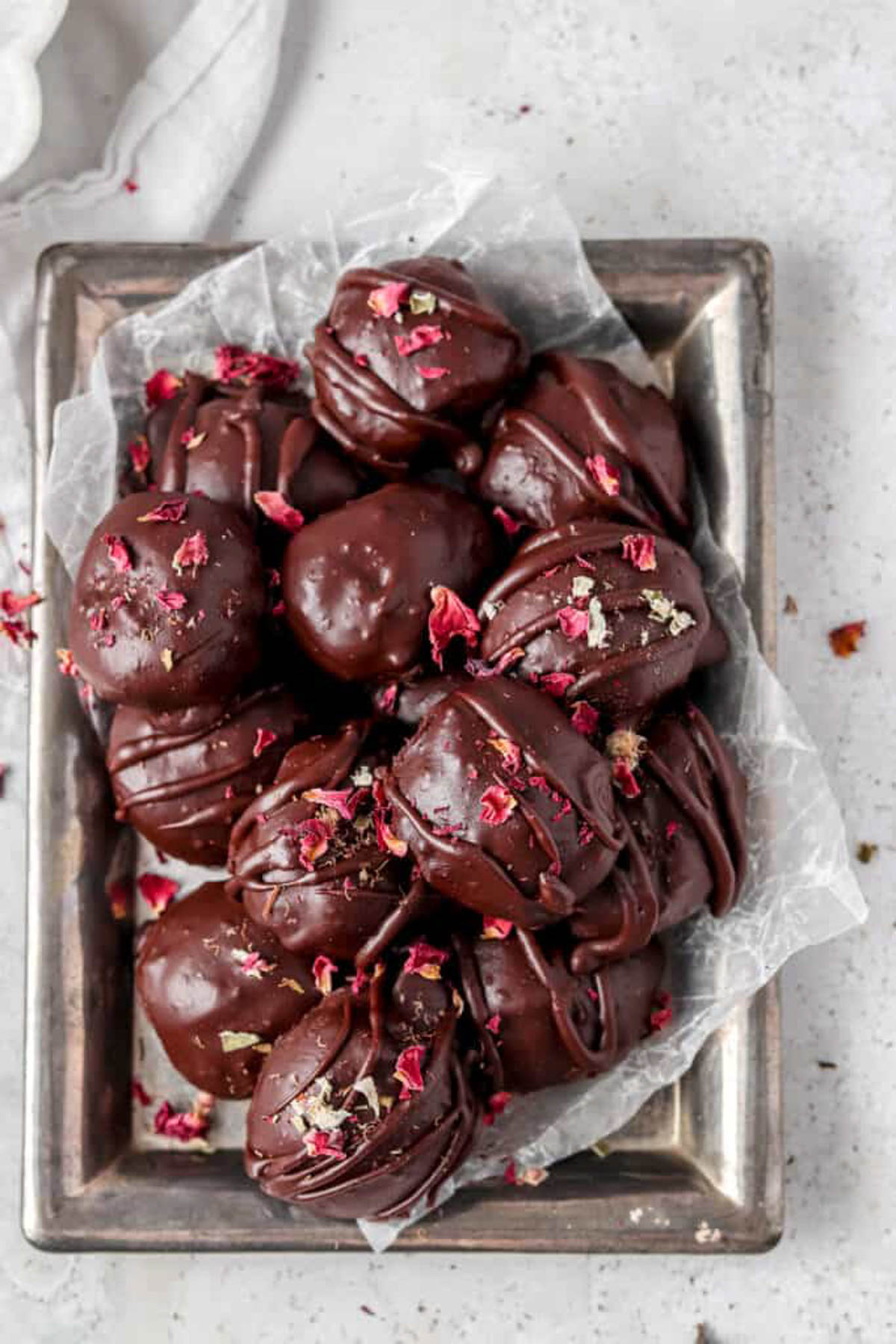 Vegan chocolate truffles stacked in metal tin with wax paper.