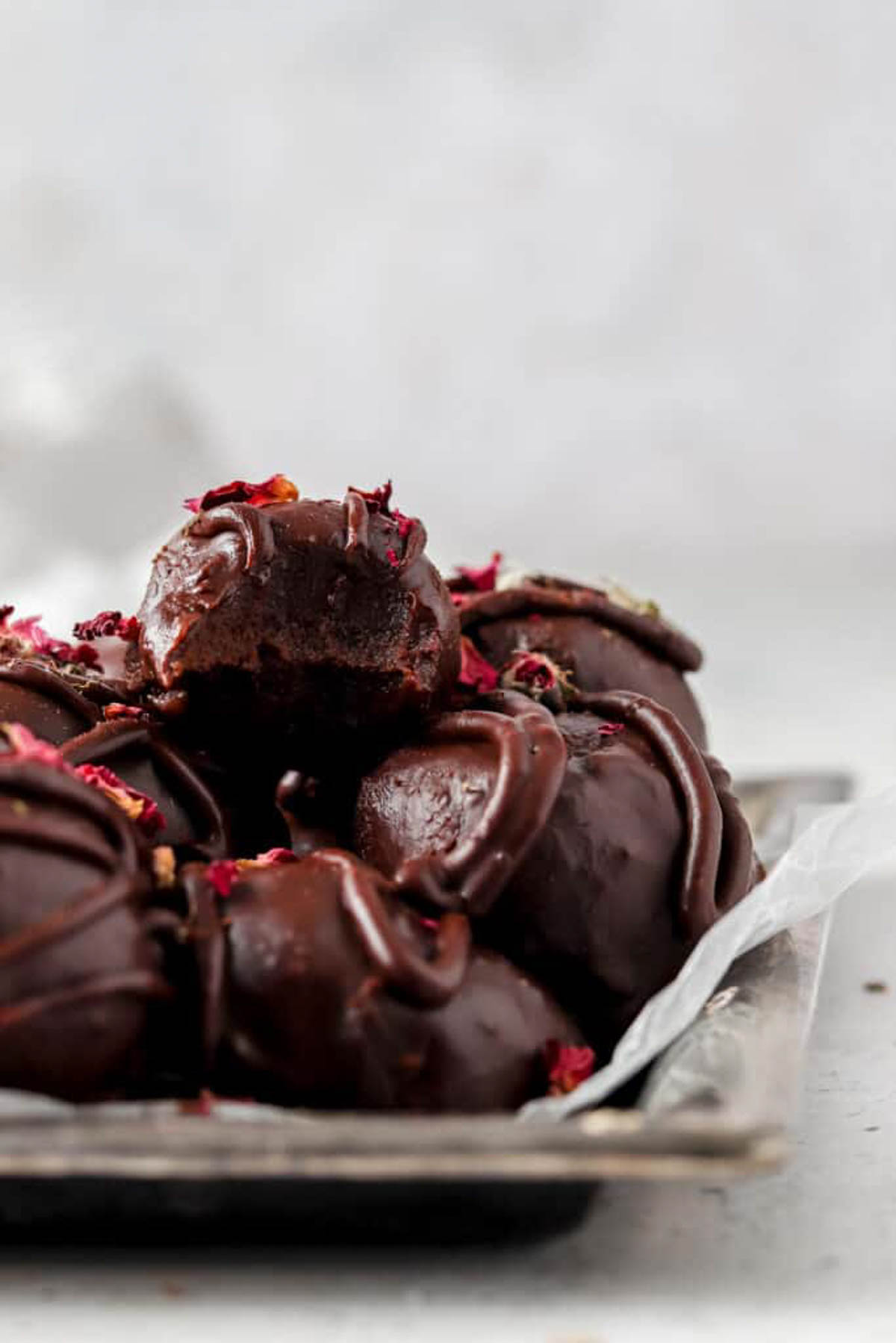Stack of vegan chocolate truffles on a plate with a truffle that has a bite taken out of it.