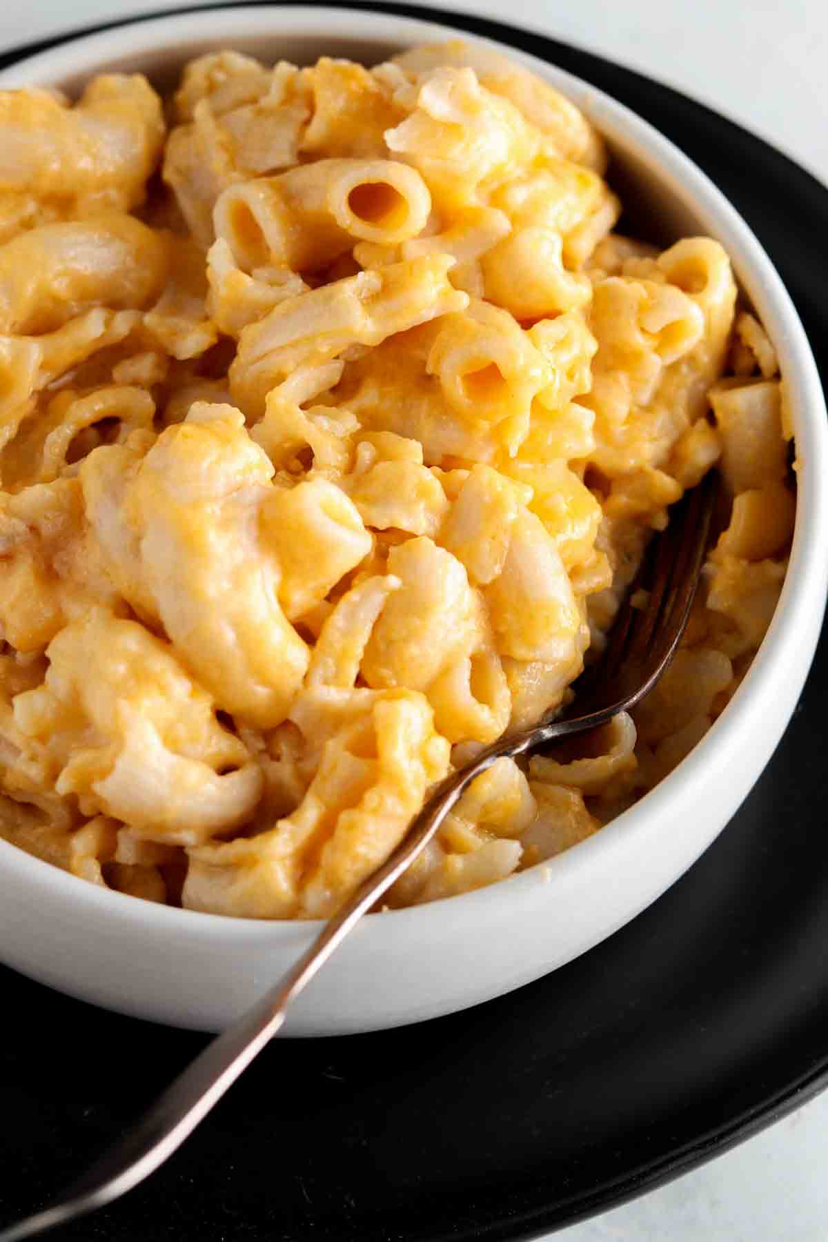 Crockpot gluten free mac and cheese in a white bowl on a plate plate with a fork in it.