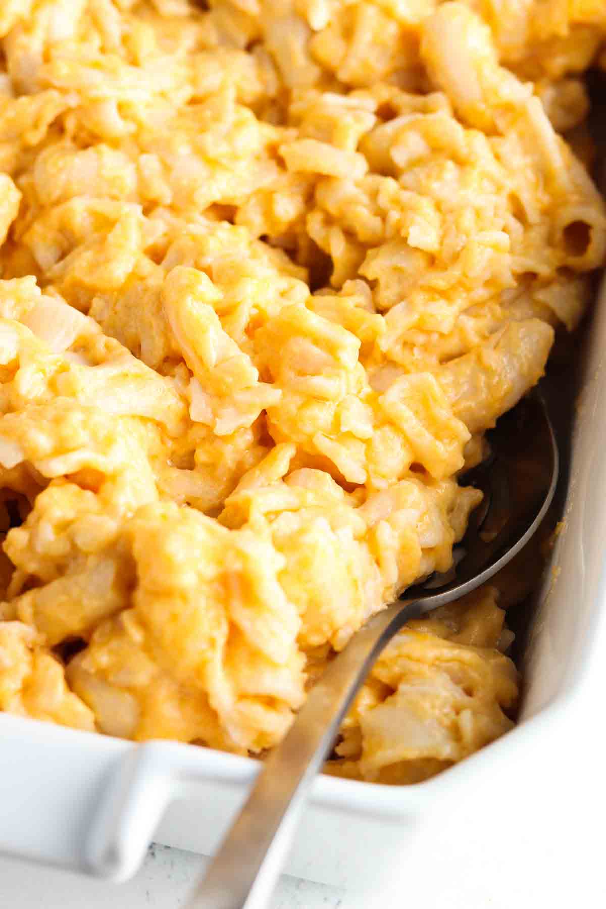 Gluten free mac and cheese in a white casserole dish with a metal serving spoon.