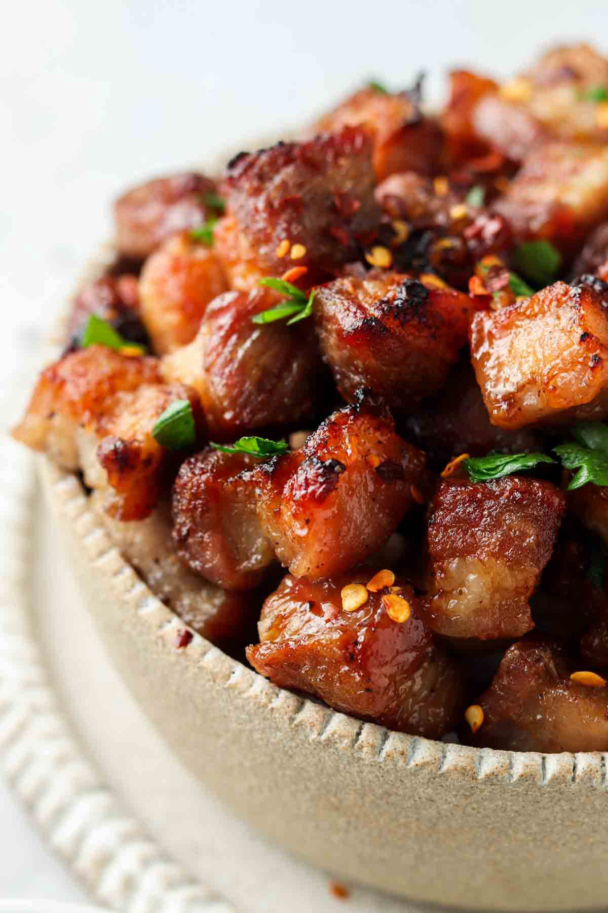 Air fryer pork belly in a bowl with fresh herbs and red pepper flakes sprinkled on top.