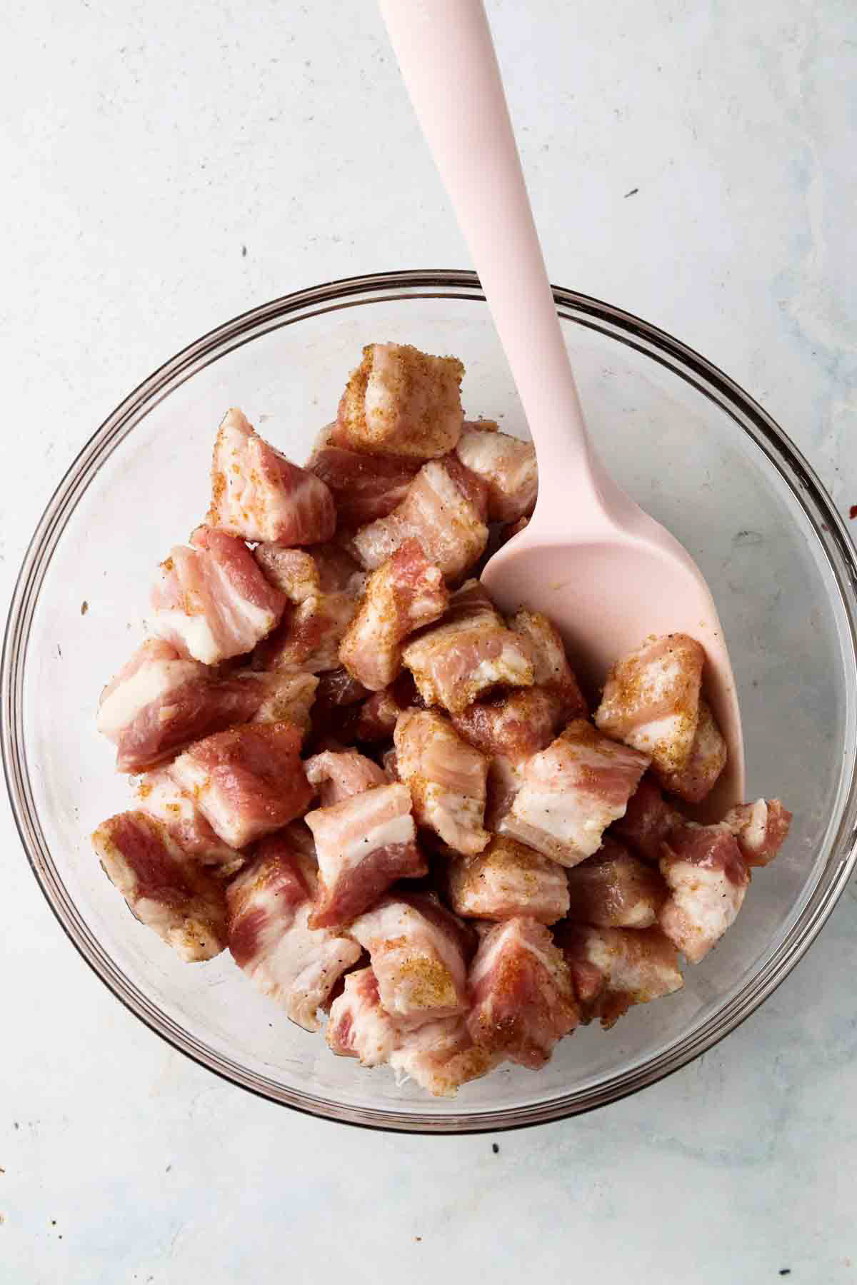 Marinated belly in a glass bowl with a pink spatula mixed well throughout. 