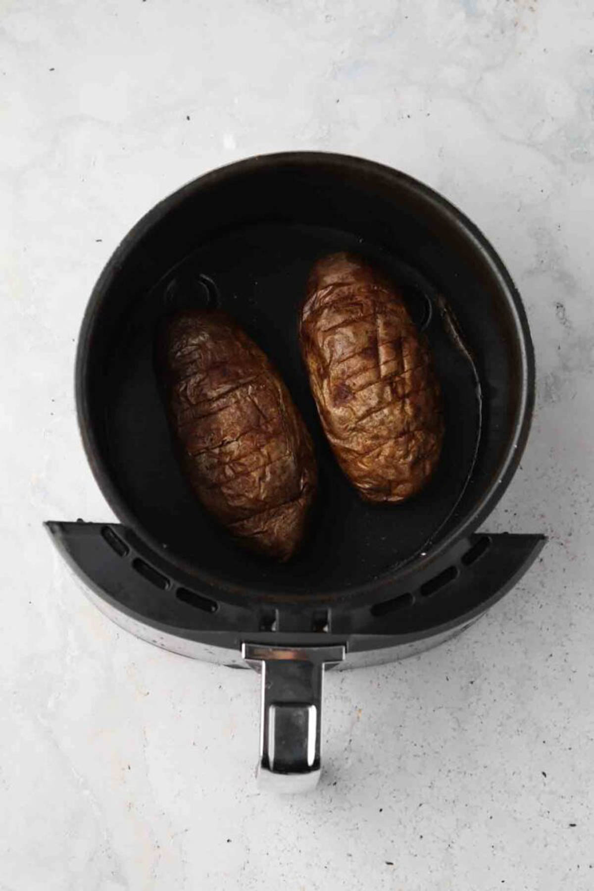 Two whole white potatoes uncooked in an air fryer basket. 