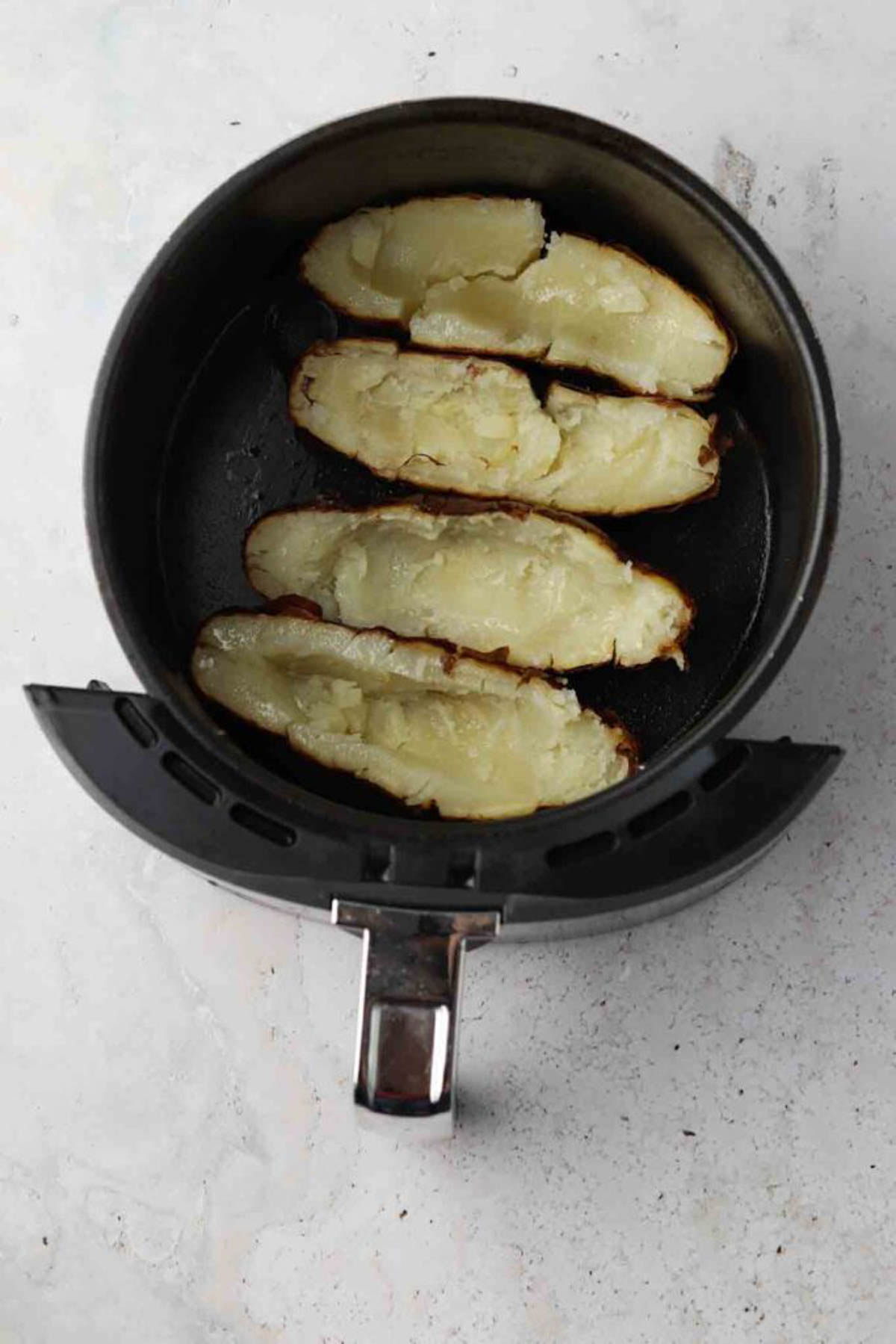 Halved baked potato skins in an air fryer basket.