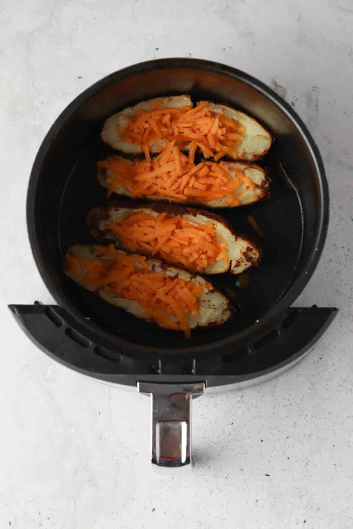 Halved potato skins in an air fryer basket with shredded cheese on top. 