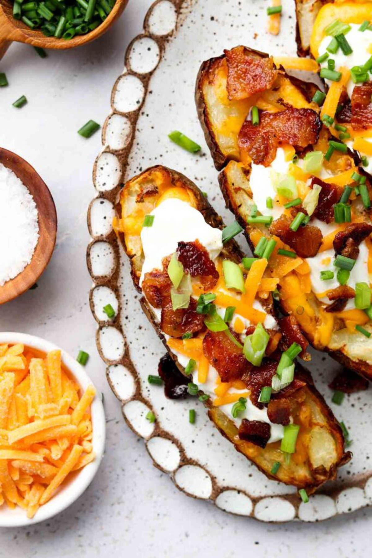 Air fryer potato skins on a plate and garnished with bacon, sour cream, and fresh green herbs.