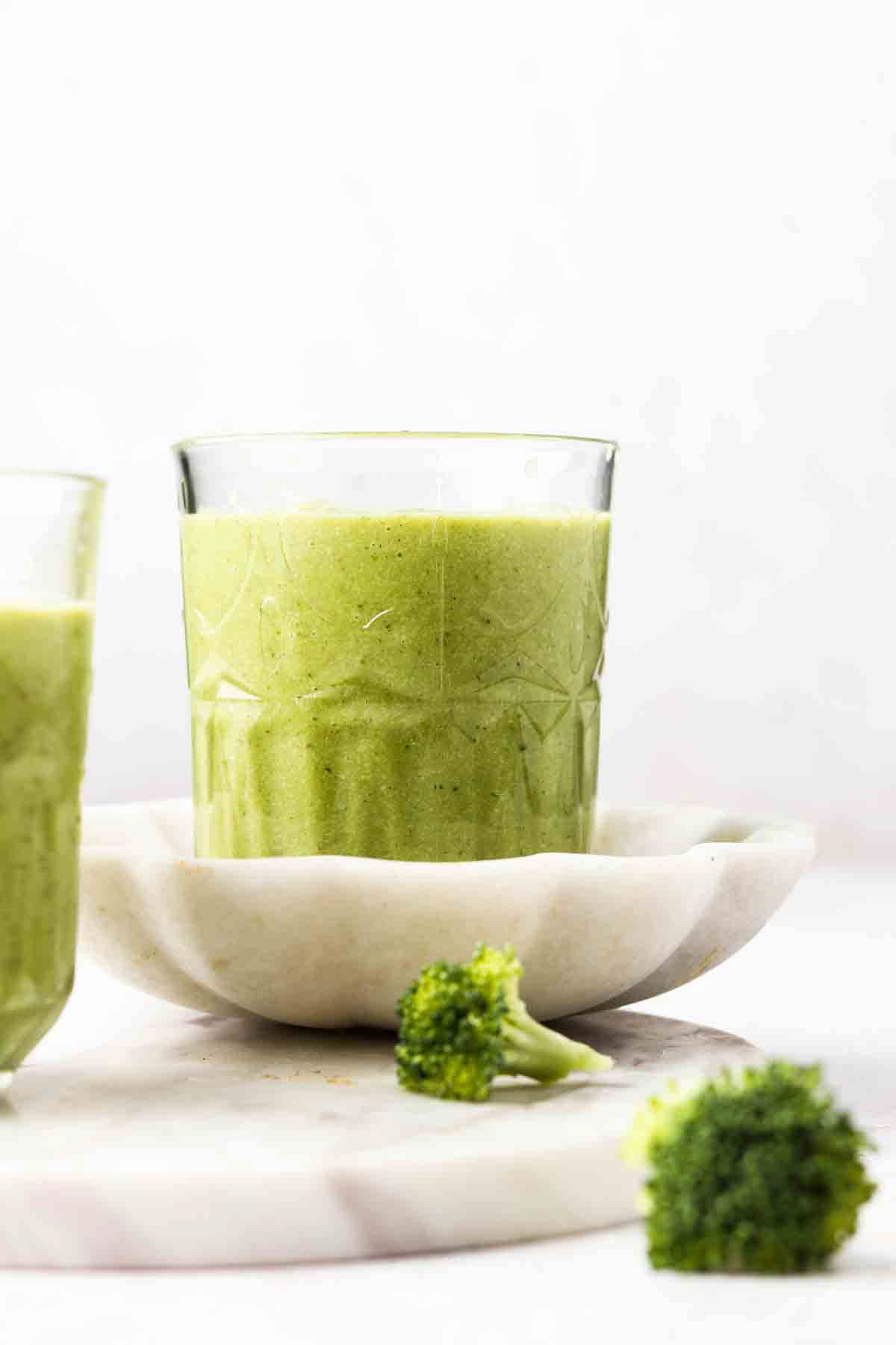 Dairy free broccoli smoothie in a glass cup on a cream plate and tray and garnished with broccoli florets.