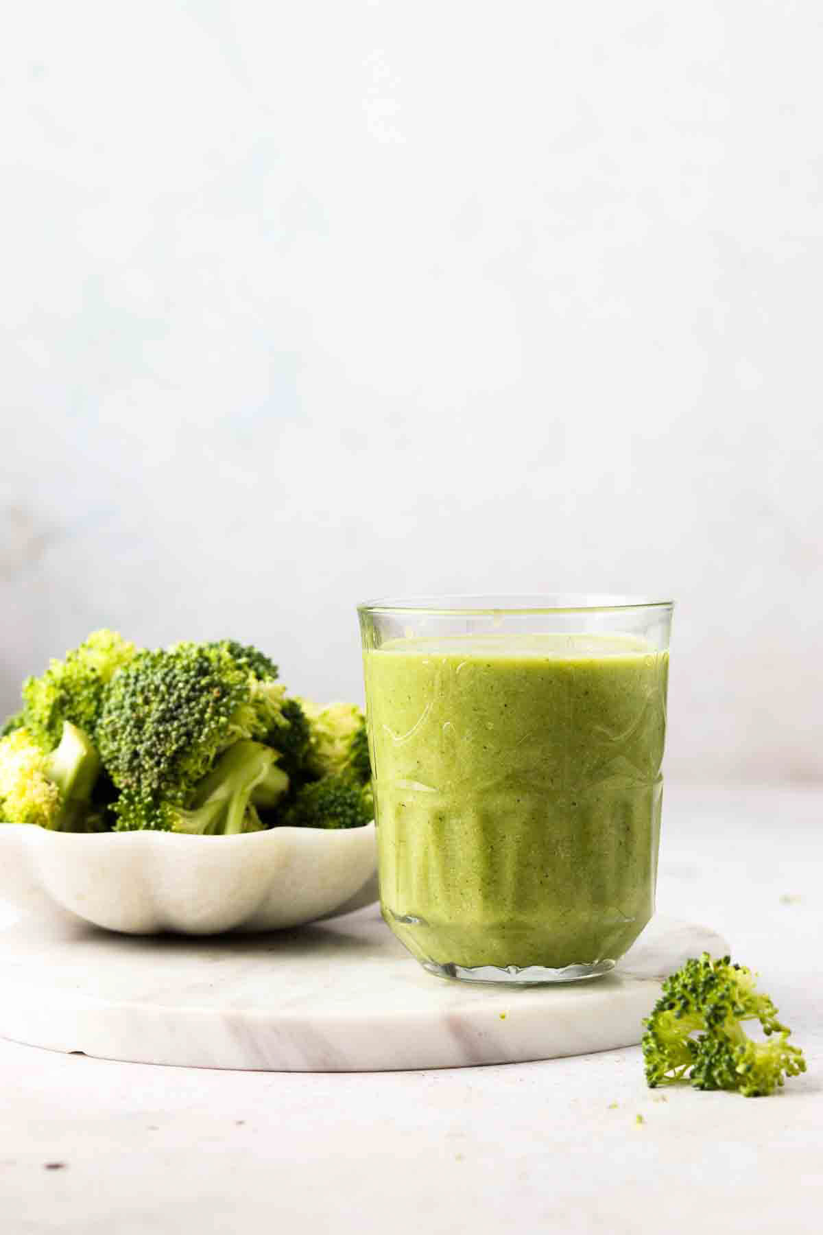 Broccoli smoothie in a glass with small bowl of broccoli florets next to it. 