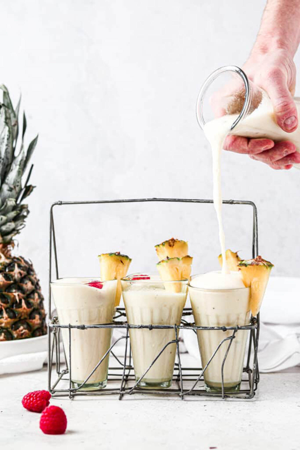 Six pina colada smoothies in a rack with the final one still being poured into.