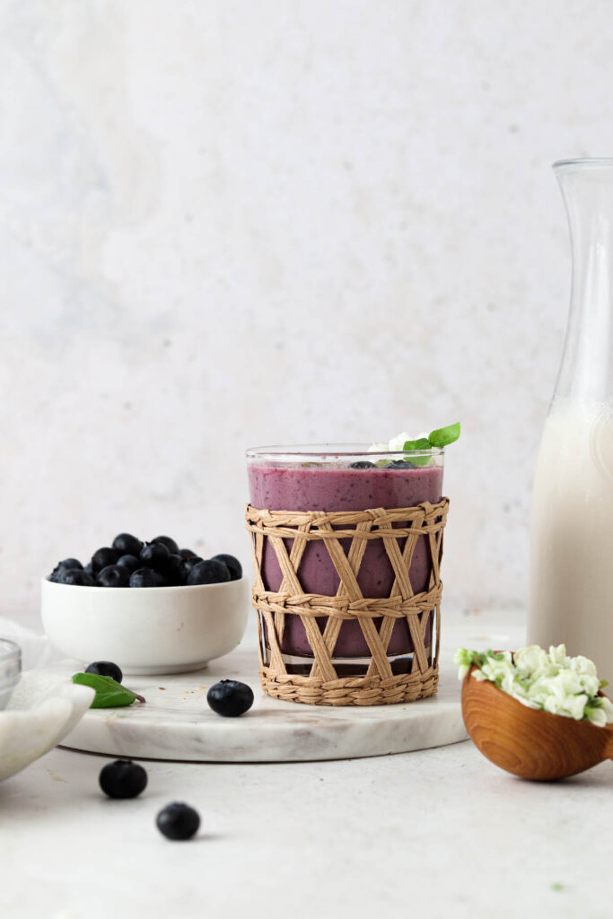 Strawberry blueberry smoothie in a glass cup with a bowl with fresh blueberry behind it.