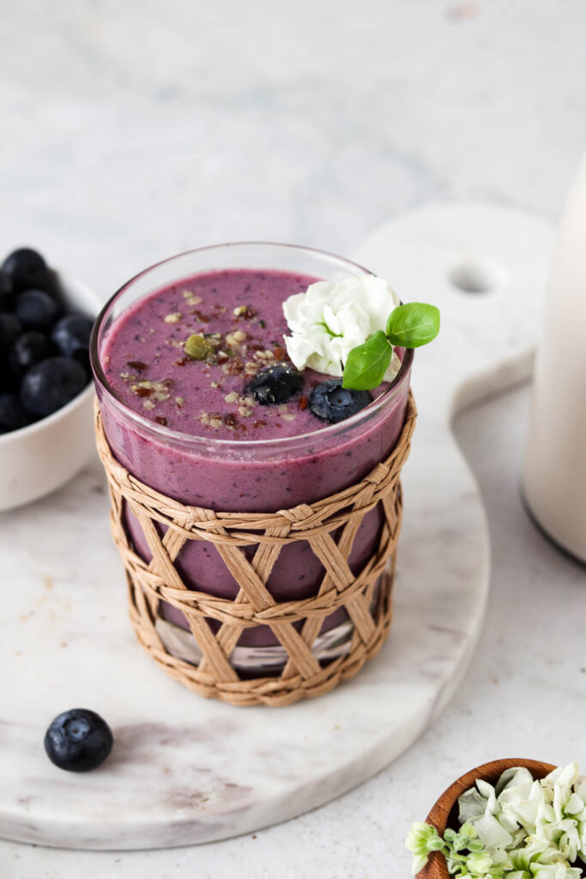 Strawberry blueberry smoothie in a glass cup garnished with seeds, fresh blueberries, and a fresh white flower.