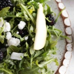 Arugula salad on a plate with pears, goat cheese, sunflower seeds and pomegranate.