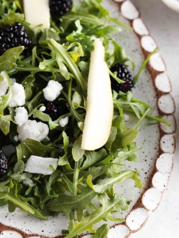 Arugula salad on a plate with pears, goat cheese, sunflower seeds and pomegranate.