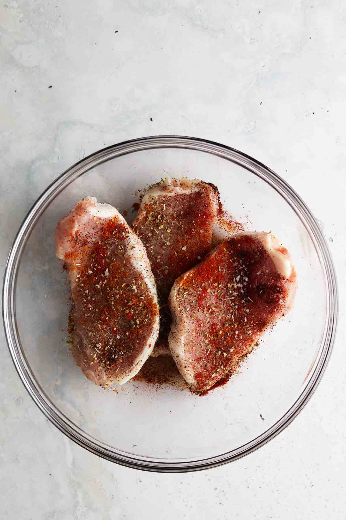 Seasoned raw pork chops in a glass bowl. 