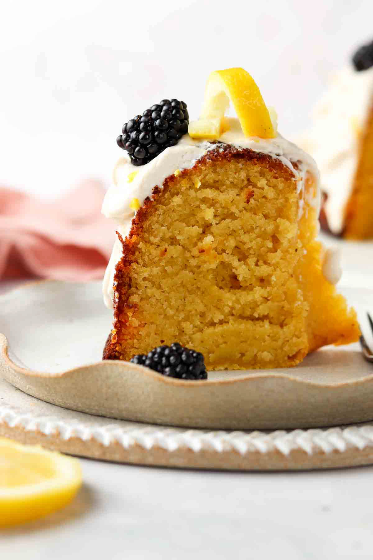 A piece of gluten free lemon cake on a plate with blackberries and lemons on top.