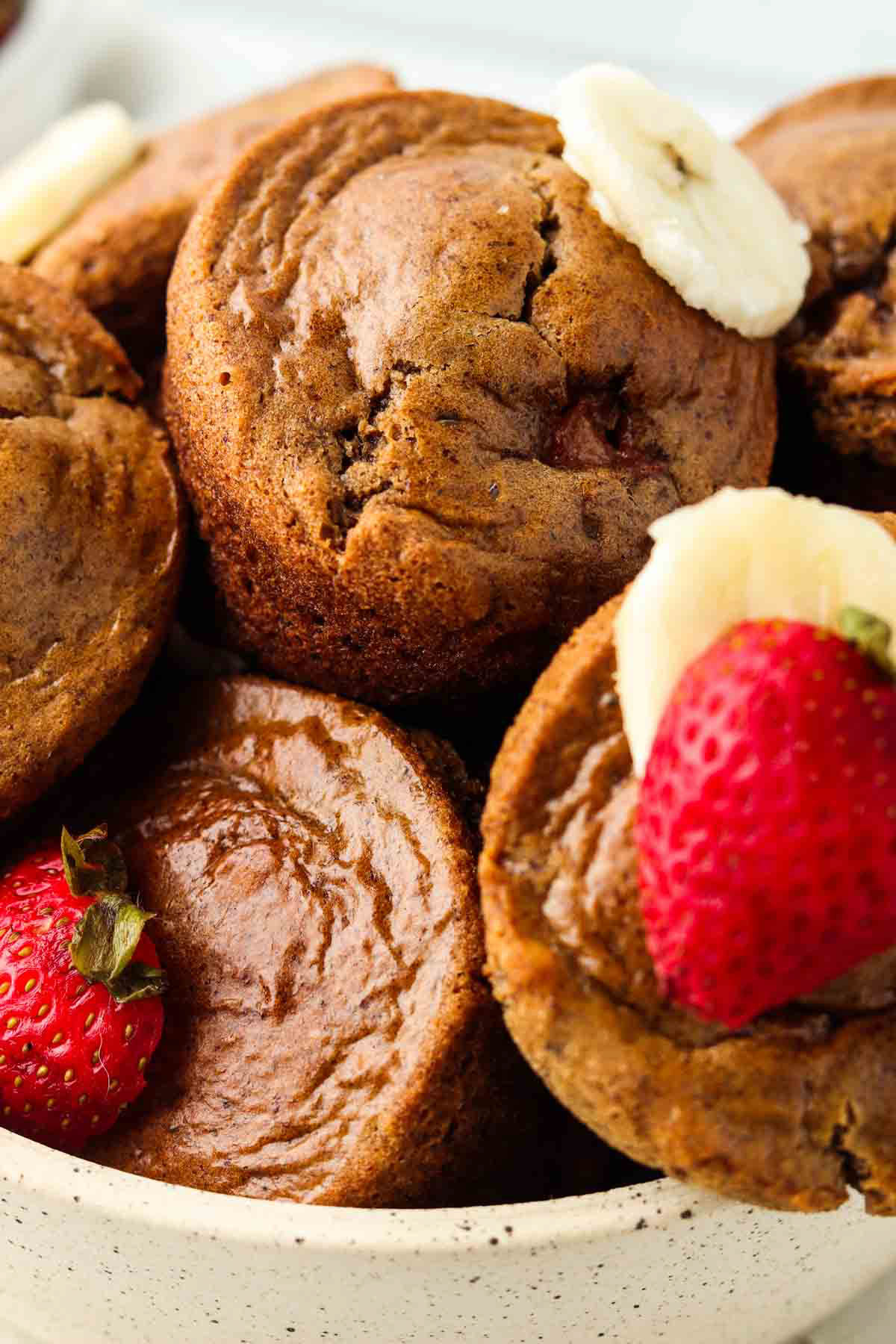 Gluten free strawberry muffins on a plate and garnished with fresh banana and strawberries. 