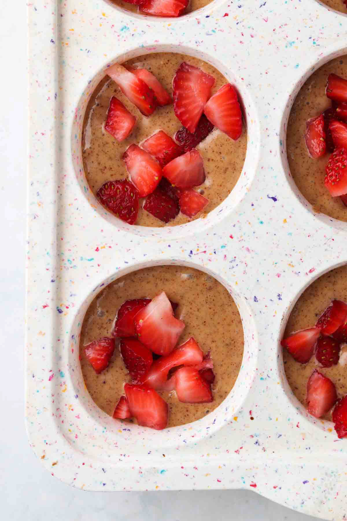 Strawberries on top of strawberry muffin batter in muffin pans.