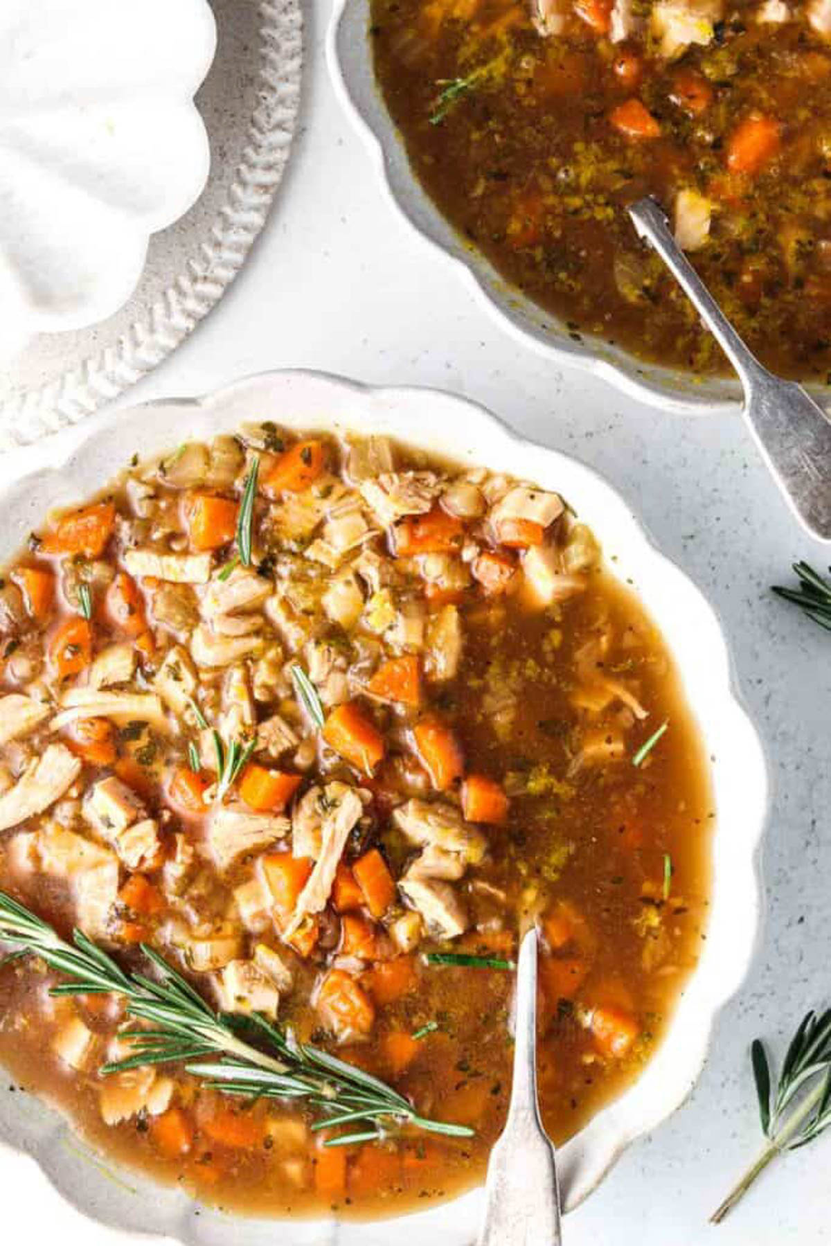 Instant pot turkey soup in a white bowl with fresh rosemary and a spoon. 