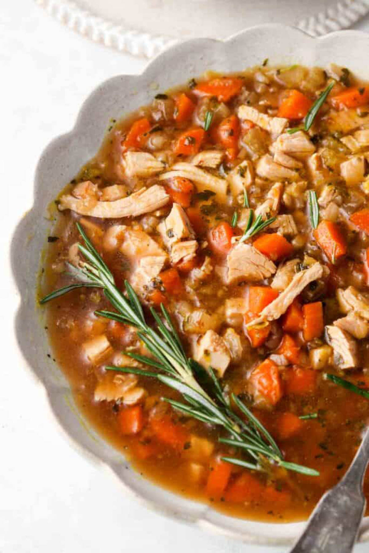 Bowl of instant pot turkey soup in a white bowl with a fresh spring of rosemary. 