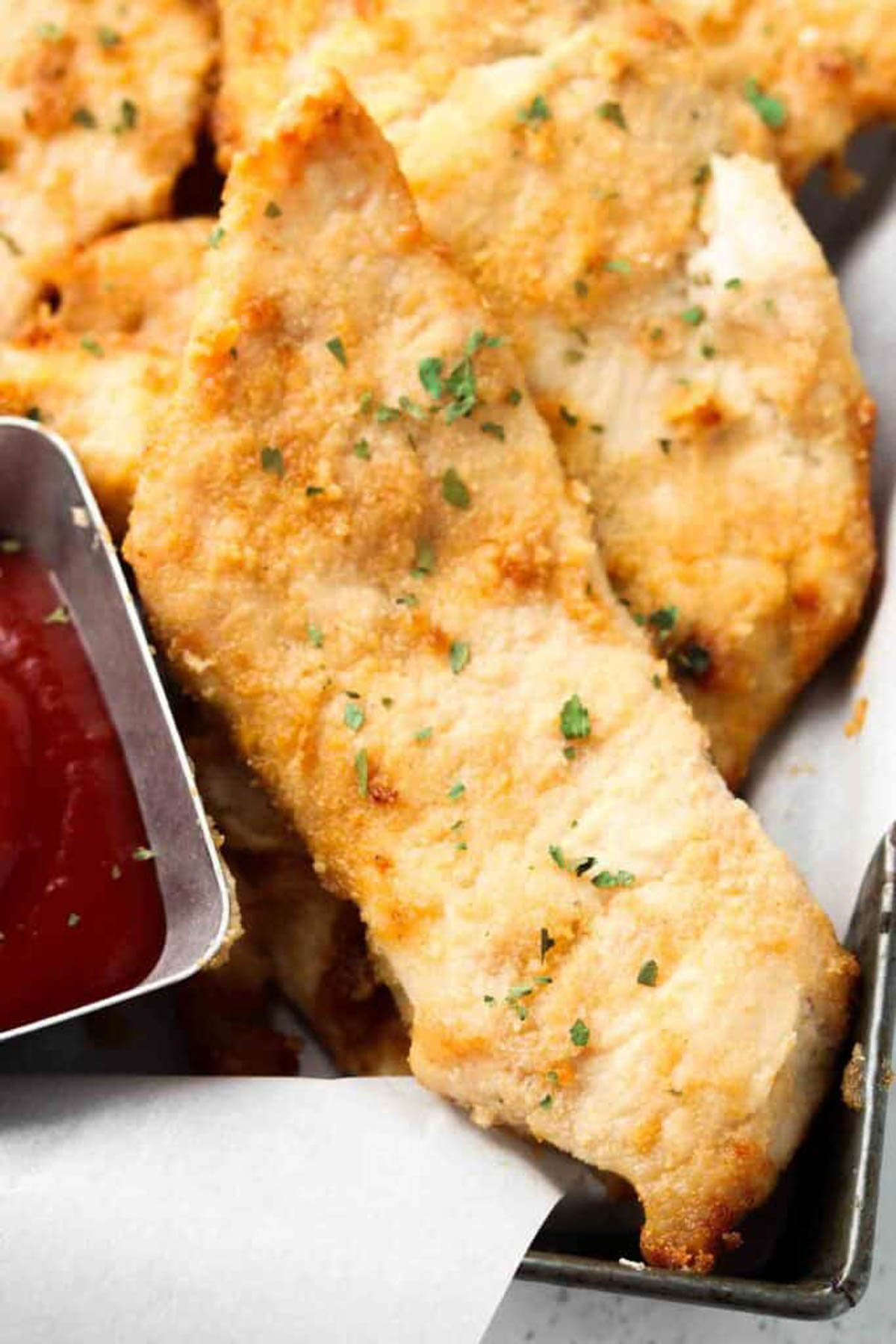 Pile of keto chicken tenders of a plate next to a bowl of dipping sauce.