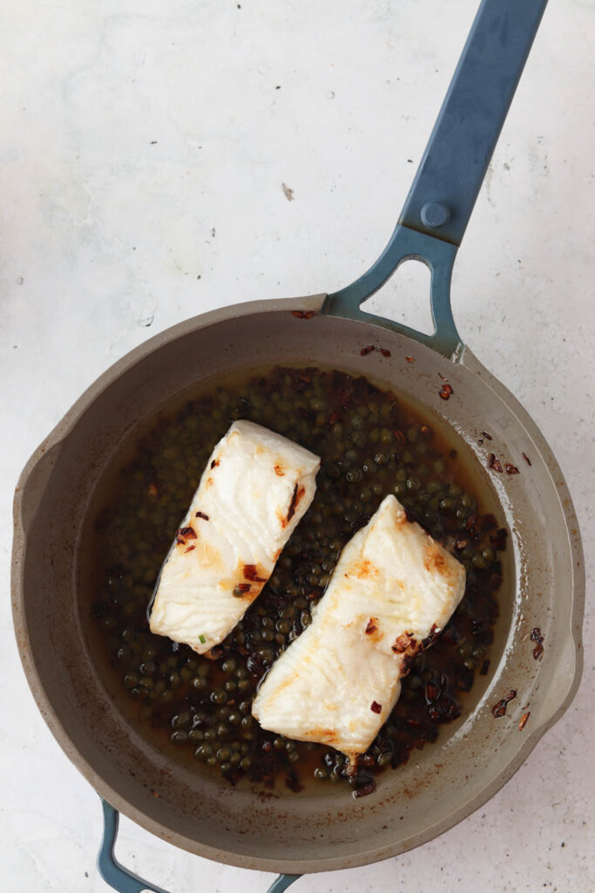 Pan seared chilean sea bass in a skillet with lemon caper sauce.