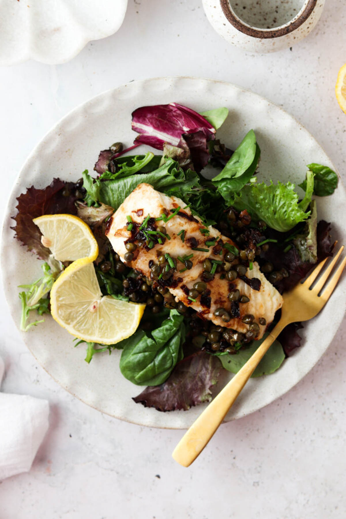 Pan seared chilean sea bass with lemon caper sauce on a bed of greens and garnished with chopped fresh green chives and lemon slices. 