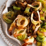 Roasted leeks on a ruffled edge plate on the counter top.