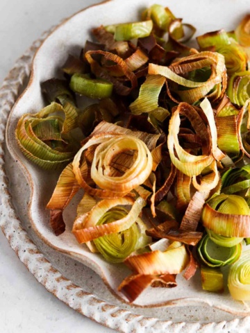 Roasted leeks on a ruffled edge plate on the counter top.