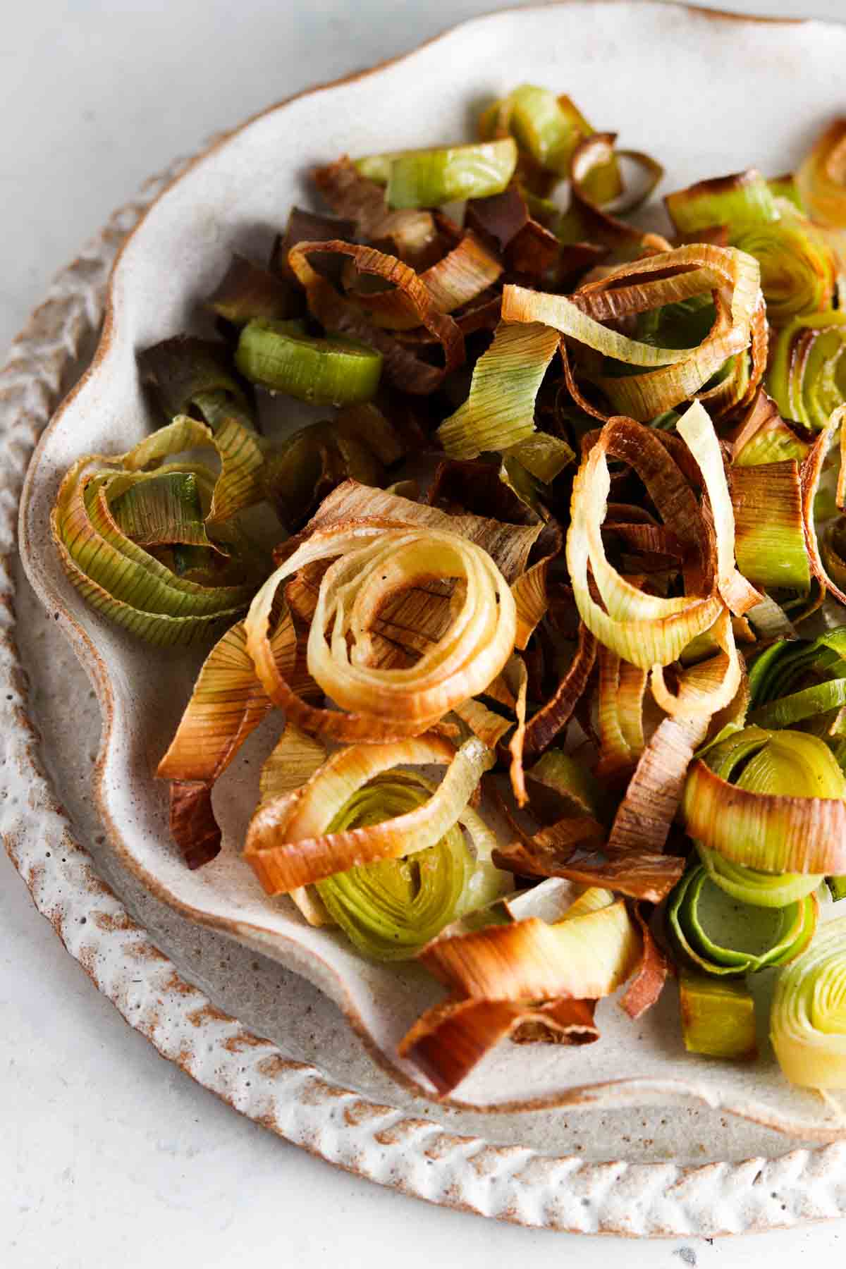 Roasted leeks on a ruffled edge plate on the counter top.