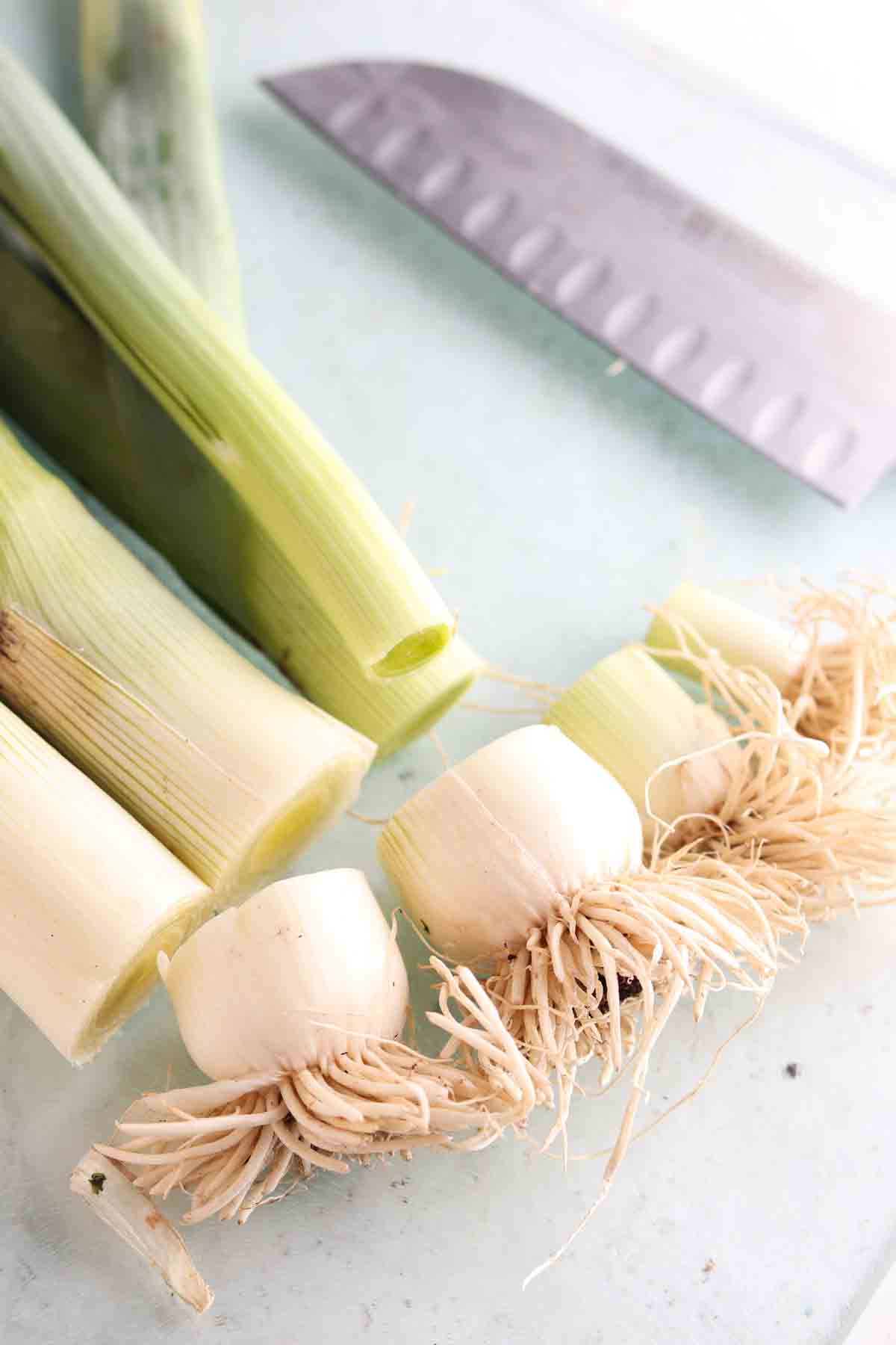 Leeks on a cutting board with the white ends cut off. 