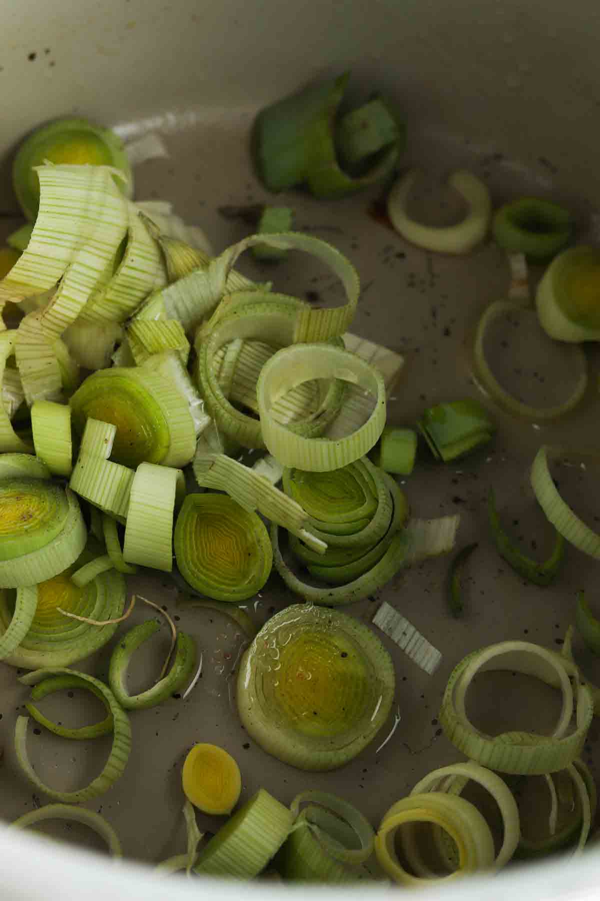 Green leeks chopped up in the air fryer with olive oil and seasoning on top.