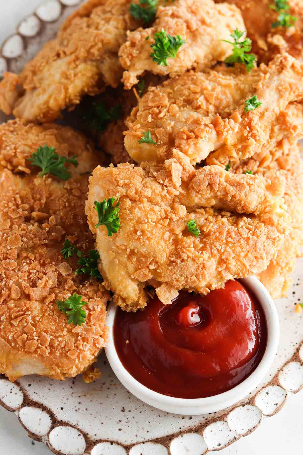 Overhead shot of gluten free chicken on a white scalloped plate and a bowl of ketchup. 