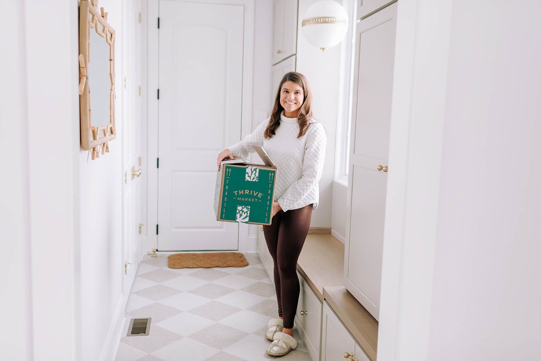 Allianna Moximchalk holding a box of Thrive Market groceries in her mud room.