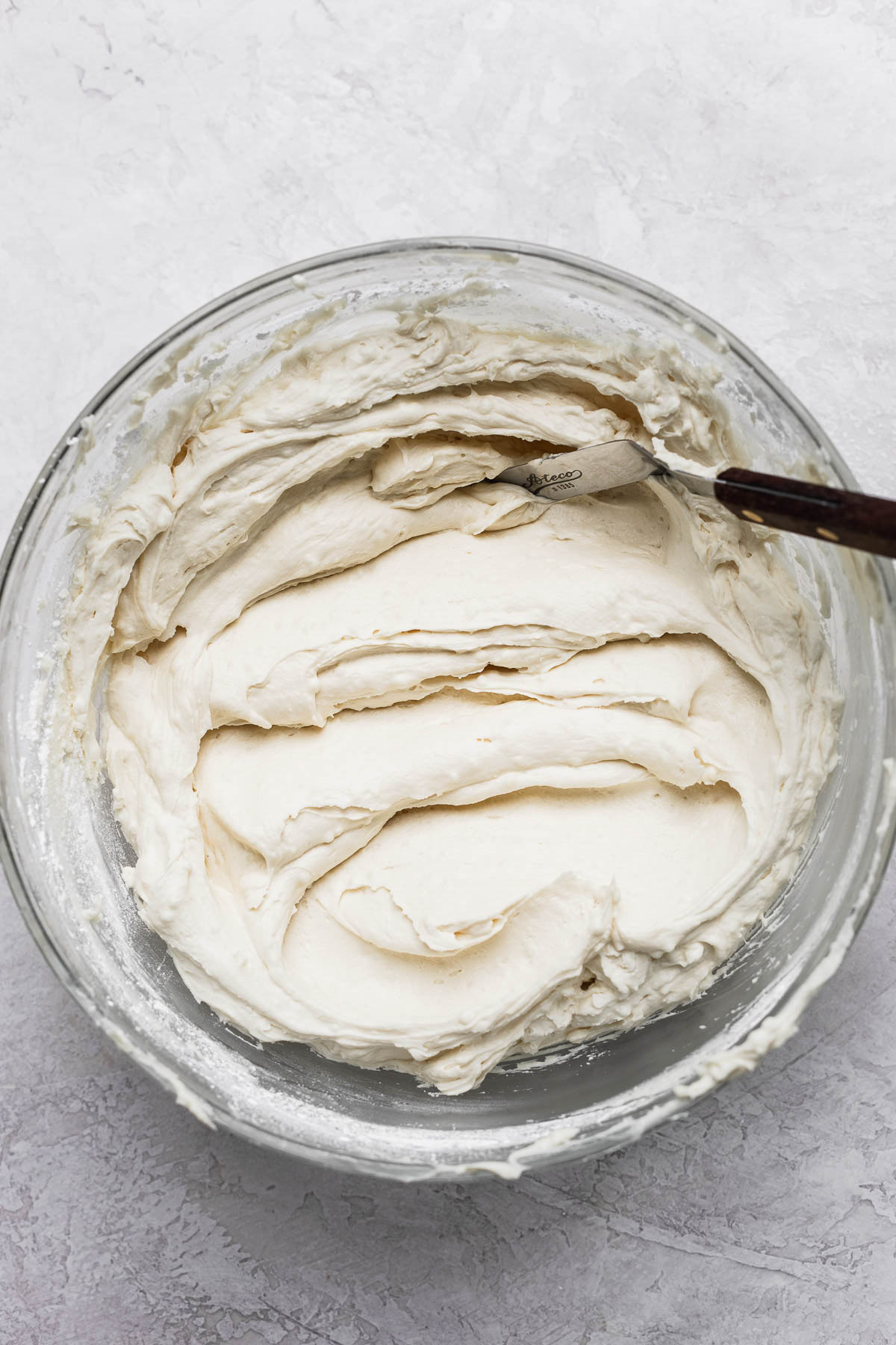 Spatula mixing the dairy free frosting in a glass bowl.