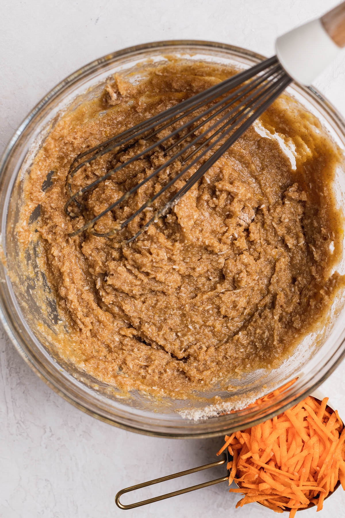 Carrot cake dry ingredients mixed with the wet ingredients in a glass bowl with a whisk.