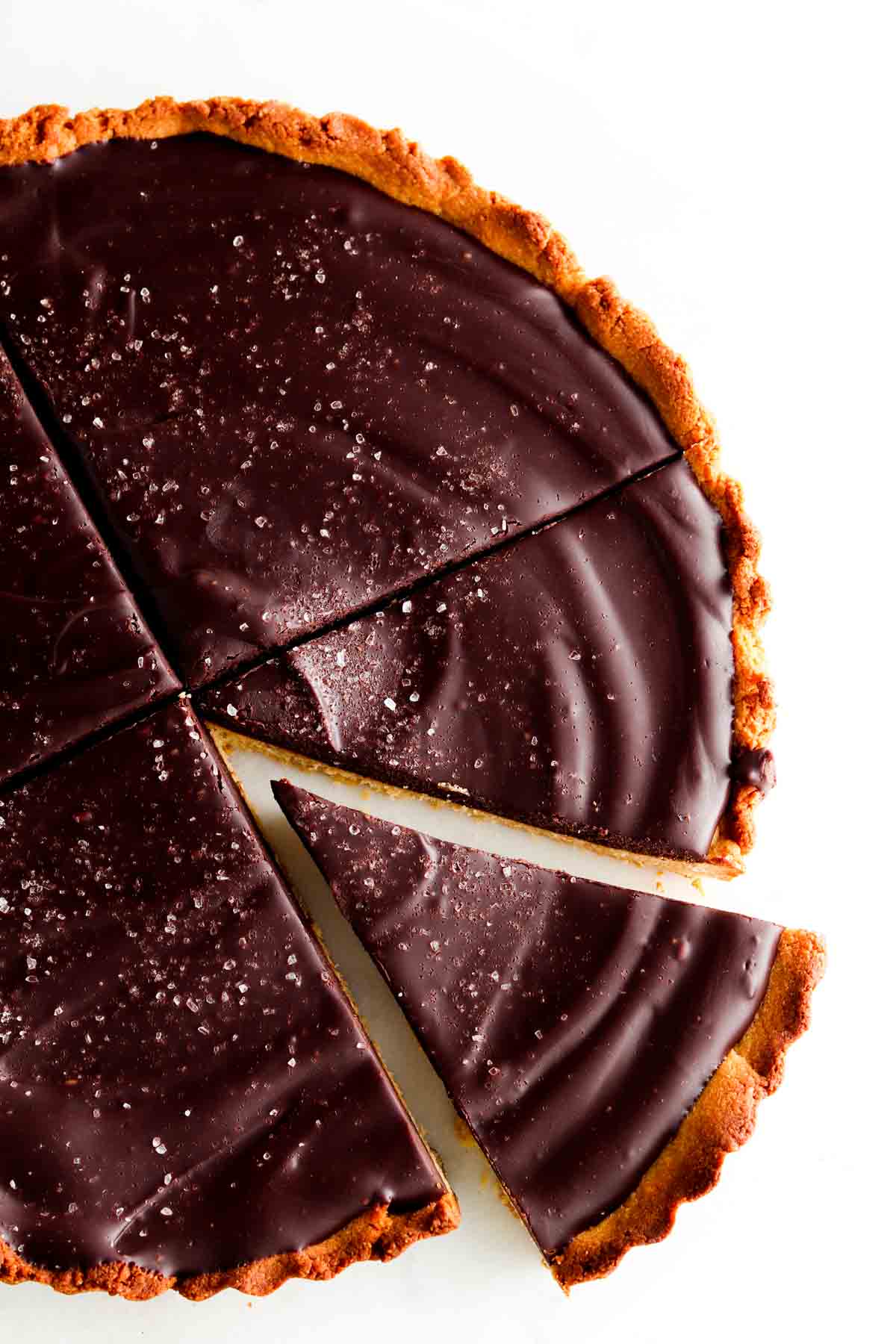 A chocolate tart on a plate with one piece cut out.