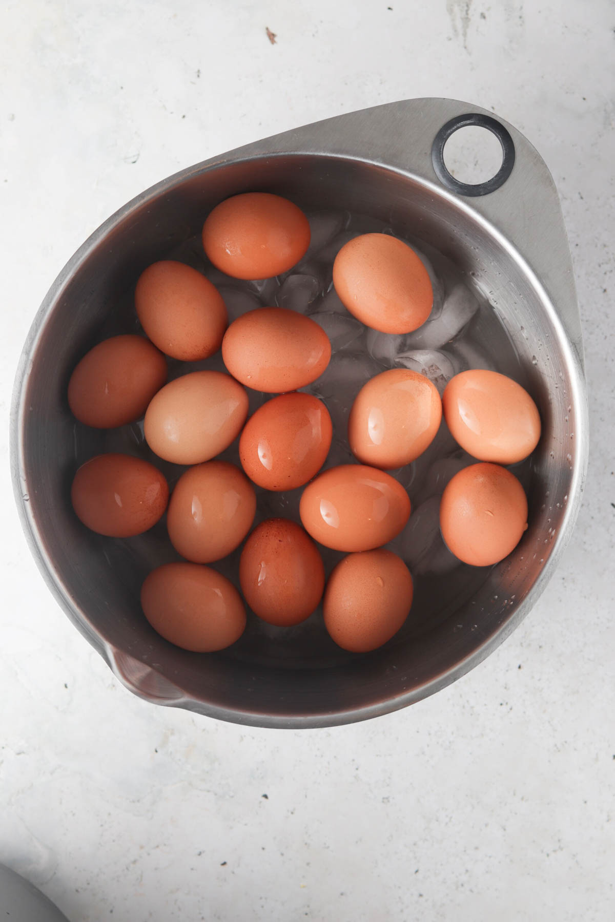 Hard boiled eggs in an ice bath in a metal bowl.