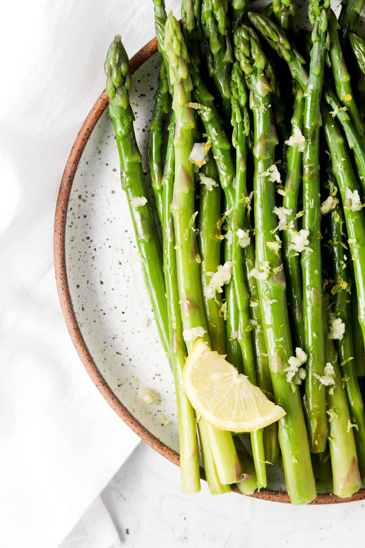 Lemon garlic asparagus on a plate with fresh garlic and a lemon slice. 