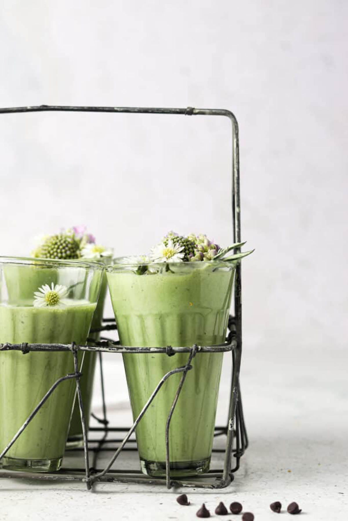 Mint smoothies in glass cups in a metal stand that are garnished with fresh flowers. 