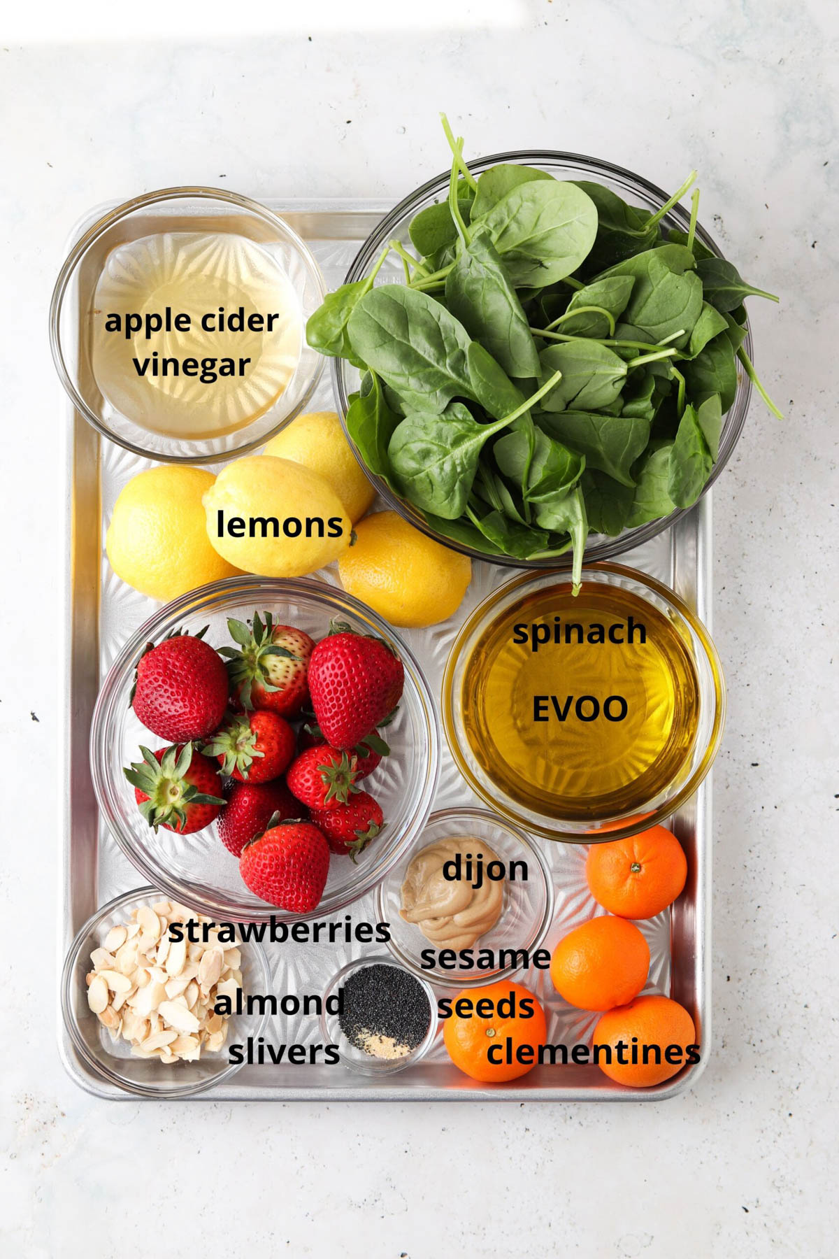 Strawberry poppyseed salad ingredients in glass bowls on a silver tray.